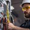 a-male-electrician-works-in-a-switchboard-with-an-2023-11-27-05-35-08-utc
